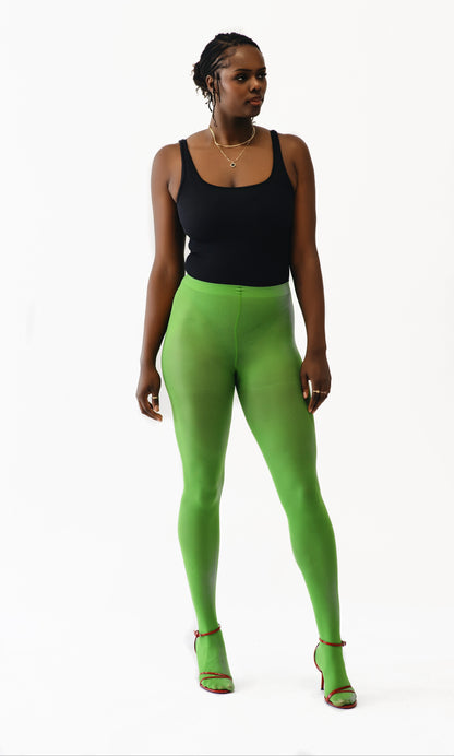 A woman modeling bright lime green full-length leggings with a black tank top and matching green high-heeled sandals, standing against a plain white studio background.